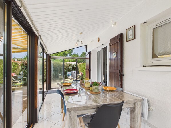 A covered patio with a glass table, chairs, and a view of the garden.