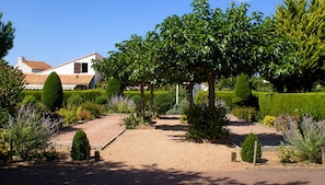 Un jardin bien entretenu, avec un chemin de gravier menant à une maison dont le toit est recouvert de tuiles.