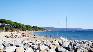Ein Strand mit felsigem Vordergrund, Menschen, die sich sonnen, und Booten im Wasser.
