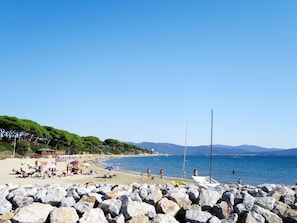 Ein Strand mit felsigem Vordergrund, Menschen, die sich sonnen, und Booten im Wasser.
