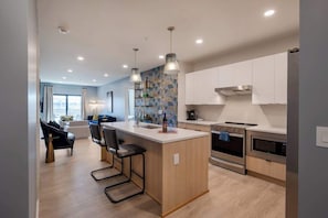 A modern kitchen with a central island, stainless steel appliances, and a dining area with a blue sofa and chairs. - 3BDR Condo for 6 Btw Broadway & Gulch|Pool,Balcony (Nashville)