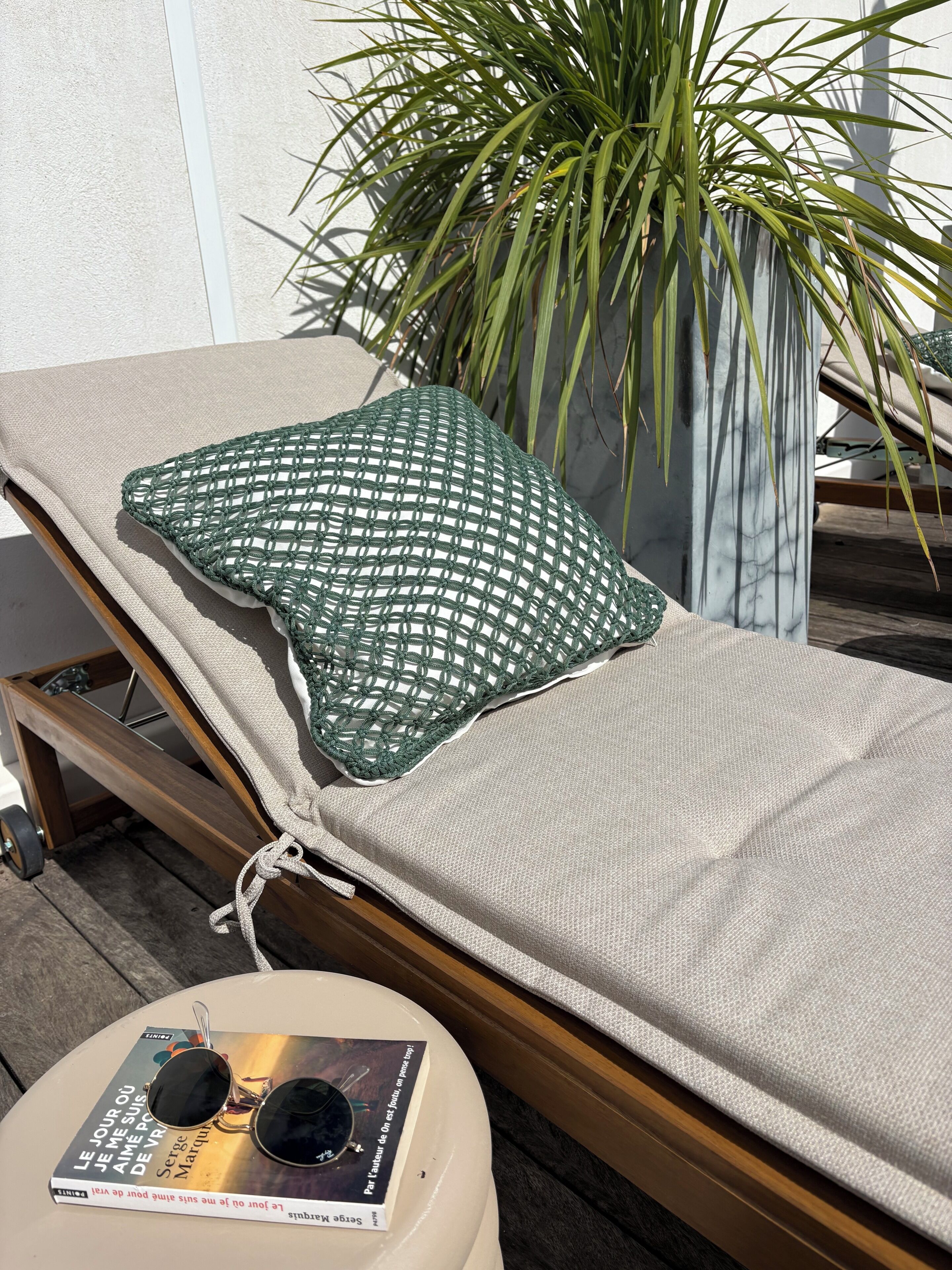 Een ligbed met een groene kussen, een boek en een zonnebril op een tafel.