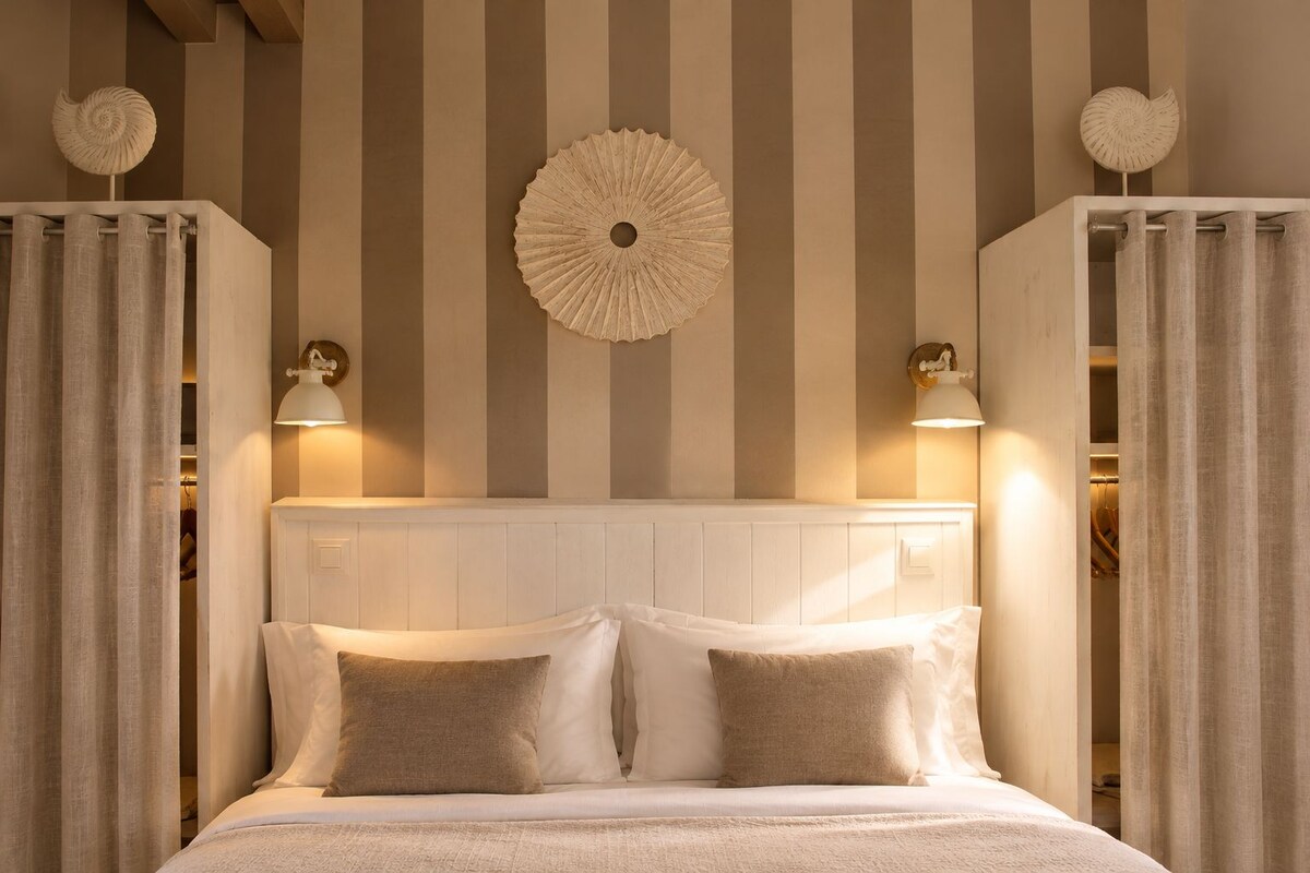 A hotel room with a large bed, striped wallpaper, decorative wall art, and two wall-mounted lamps.