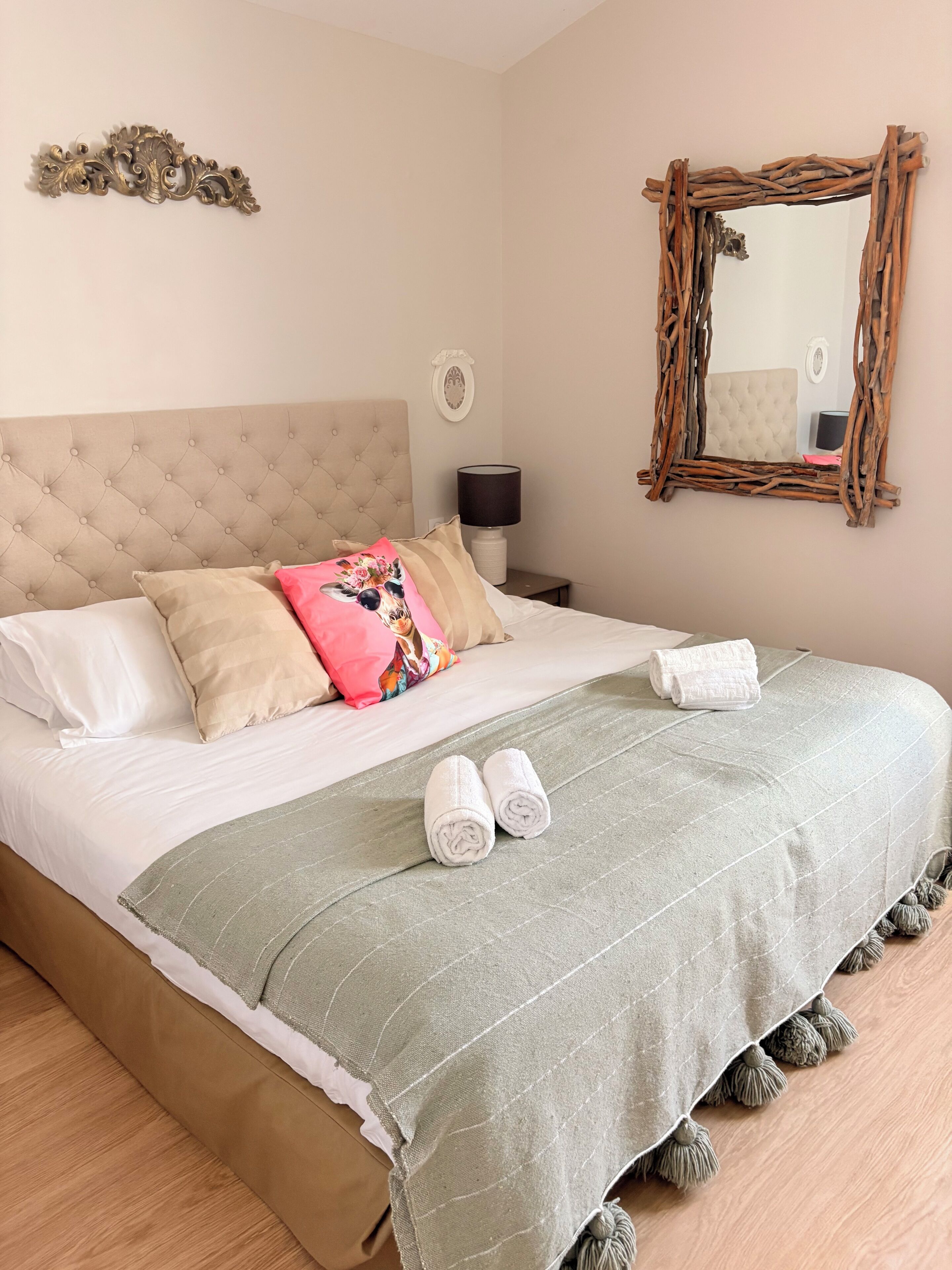 A neatly made bed with a green blanket, pillows, and rolled towels.