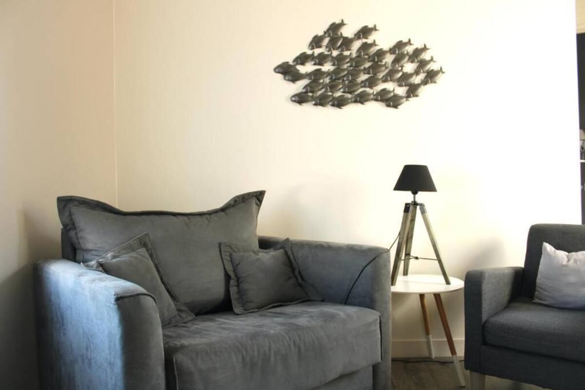 A living room with a grey sofa, a small side table with a lamp, and a wall art piece.