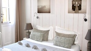 Une chambre à coucher comprenant un lit, deux tables de chevet, une fenêtre et des œuvres d’art accrochées au mur.