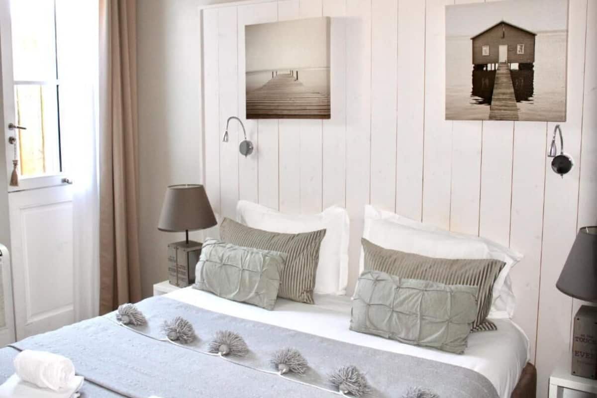 A bedroom with a bed, two bedside tables, a window, and wall-mounted artwork.