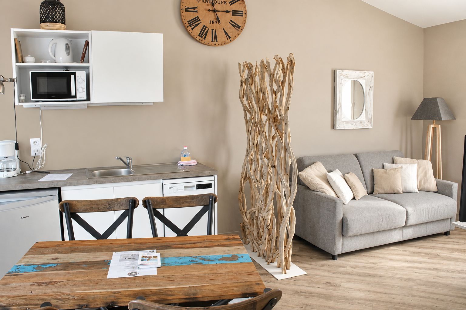 Una cocina moderna con microondas, pileta y muebles, un comedor con mesa y sillas de madera, un sofá gris y una escultura decorativa de madera.