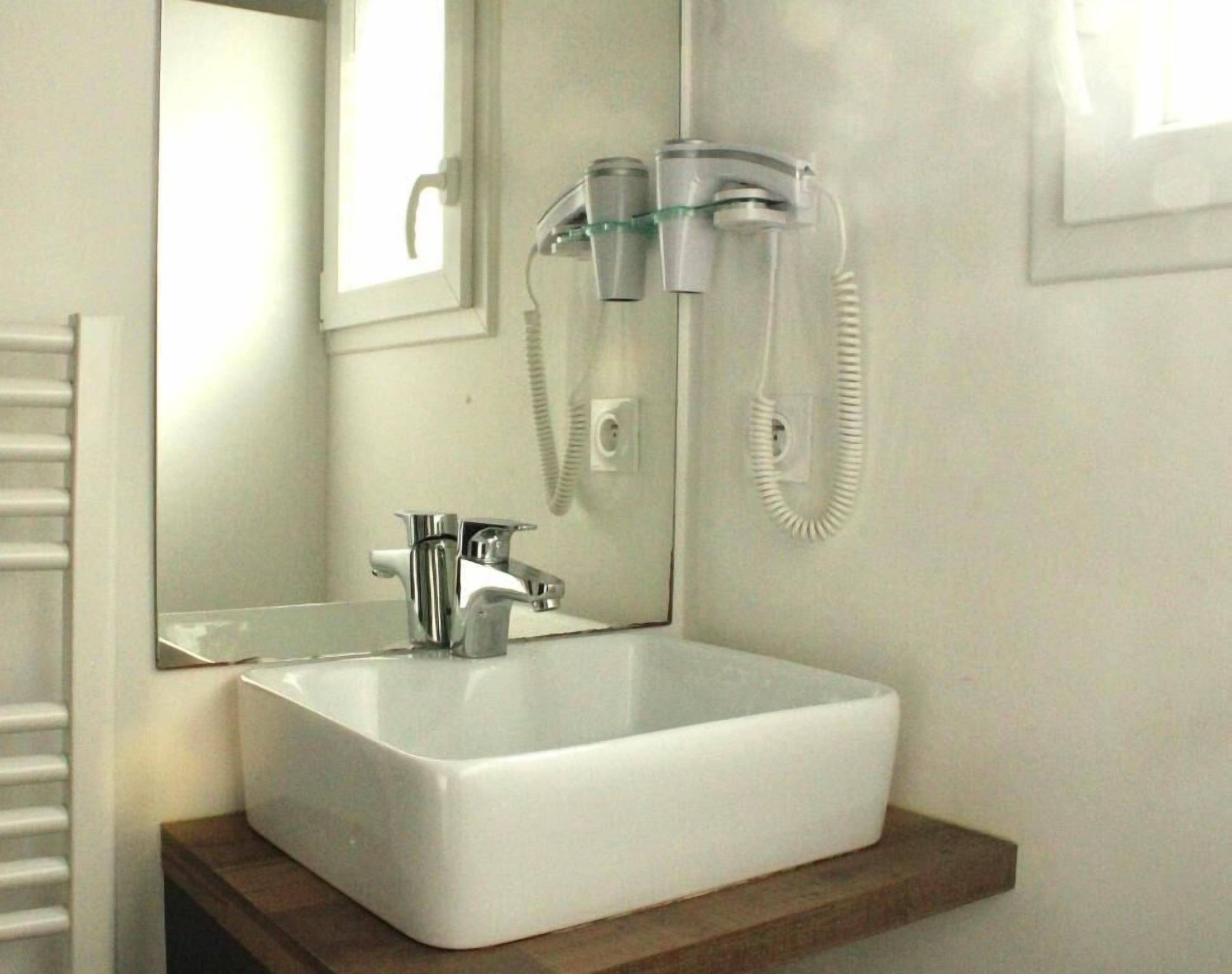 A bathroom with a white sink, a mirror, a handheld showerhead, and a towel rack.