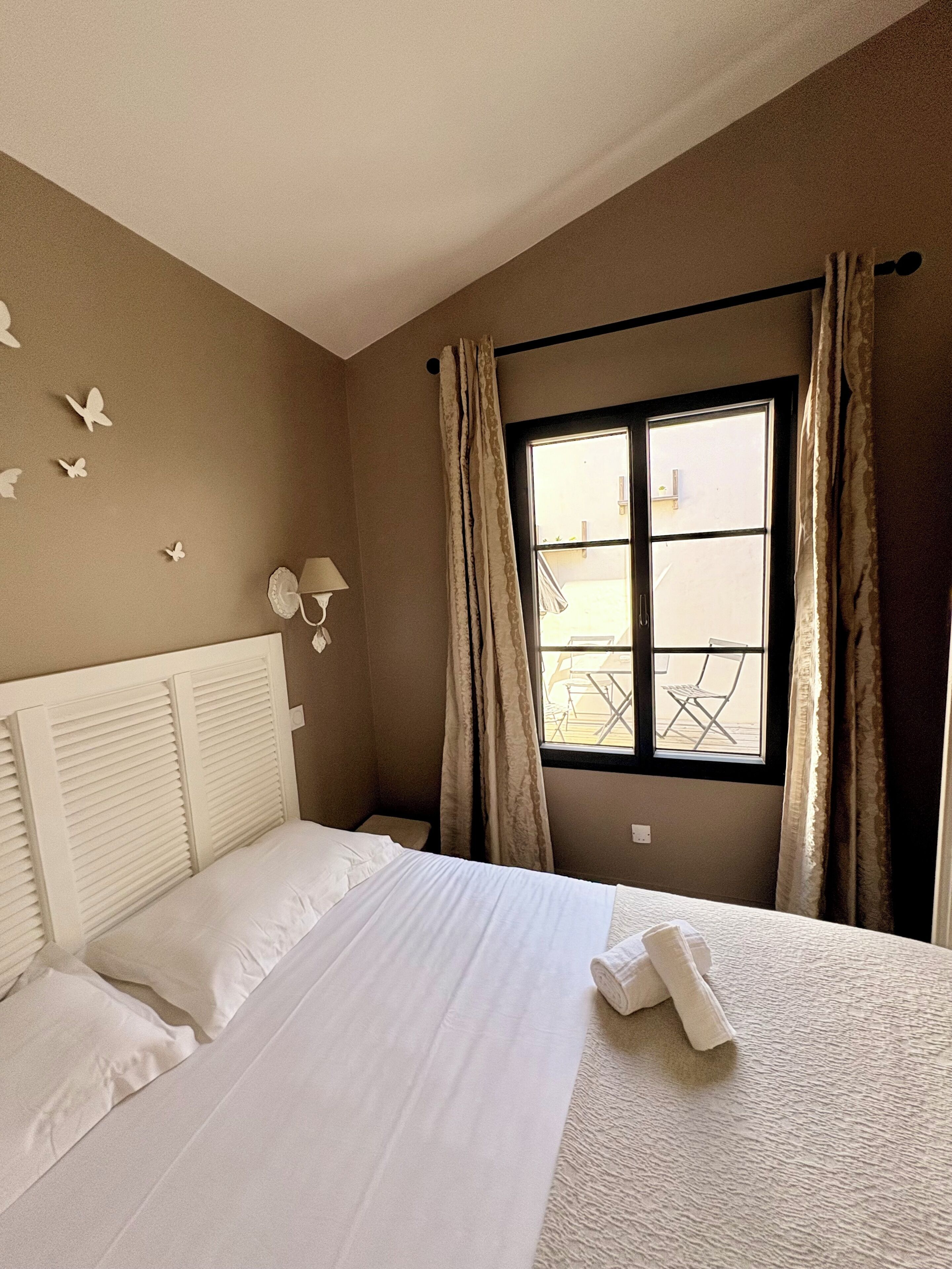 A hotel room with a bed, a window with curtains, a wall-mounted lamp, and butterfly decorations.