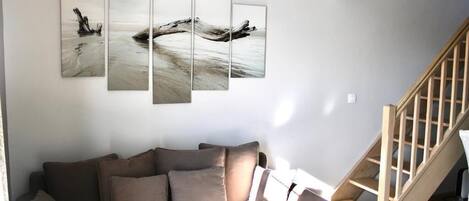 A living room with a sofa, a wooden staircase, and a wall with a multi-panel artwork.
