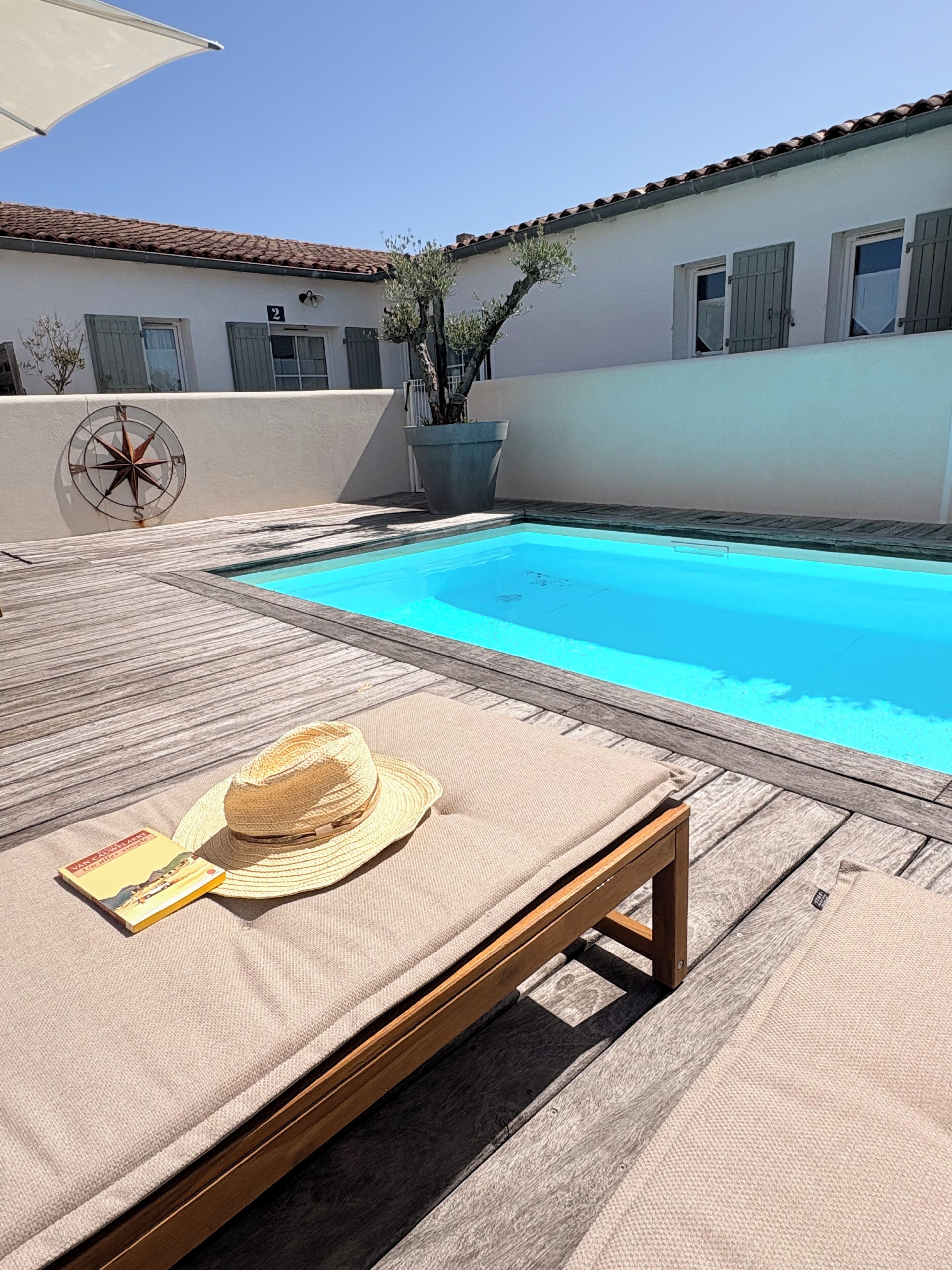 A poolside area with a lounge chair, a hat, and a book.