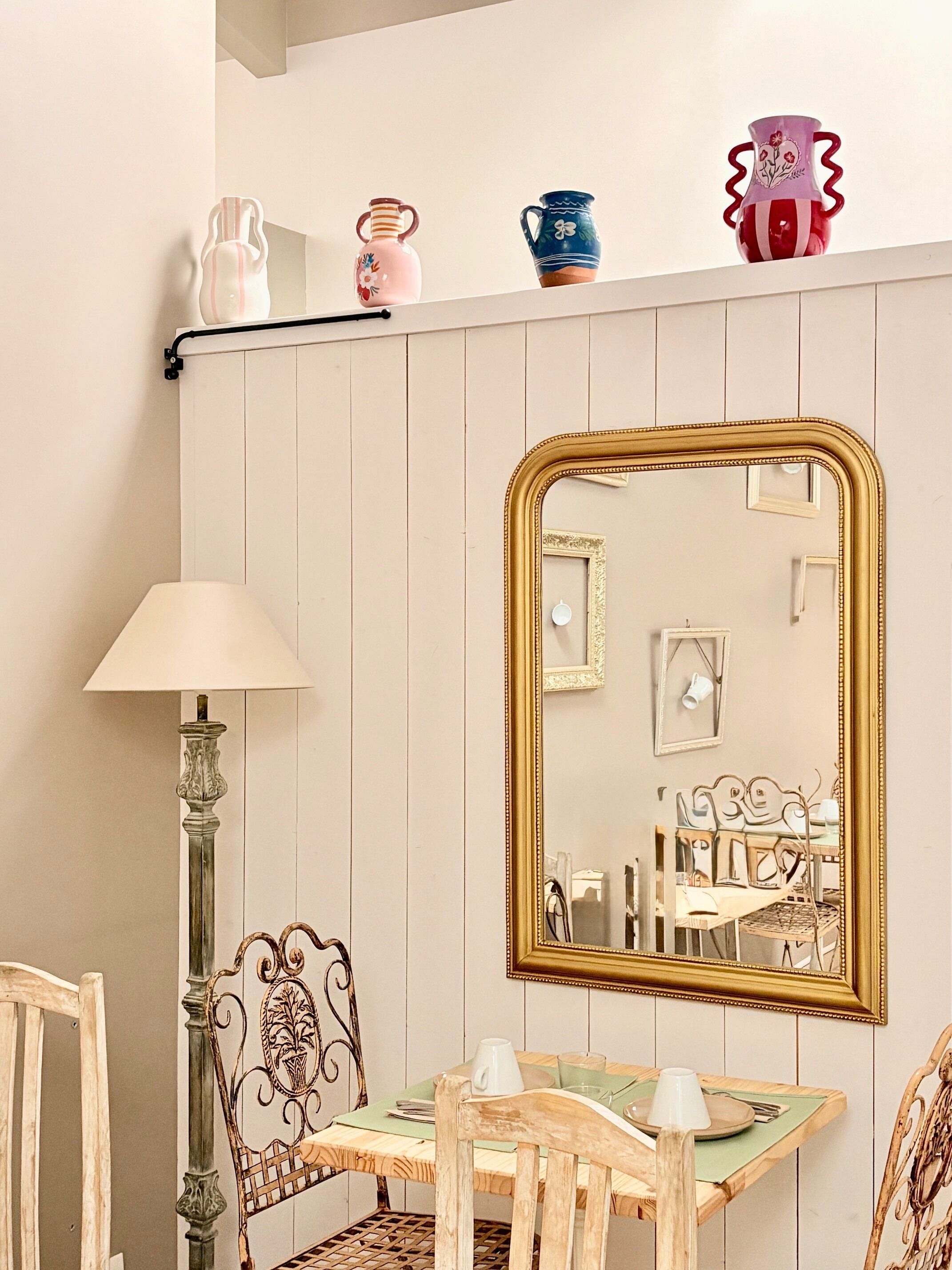 A dining area with a table, chairs, a lamp, and a mirror.