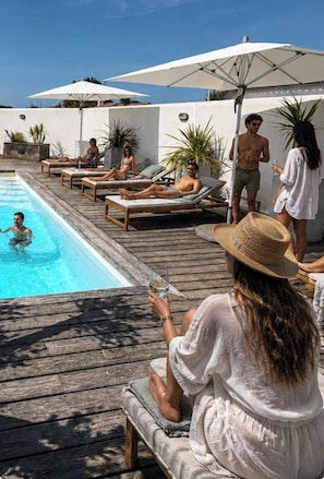 A poolside area with lounge chairs and umbrellas, a pool, and a wooden deck.
