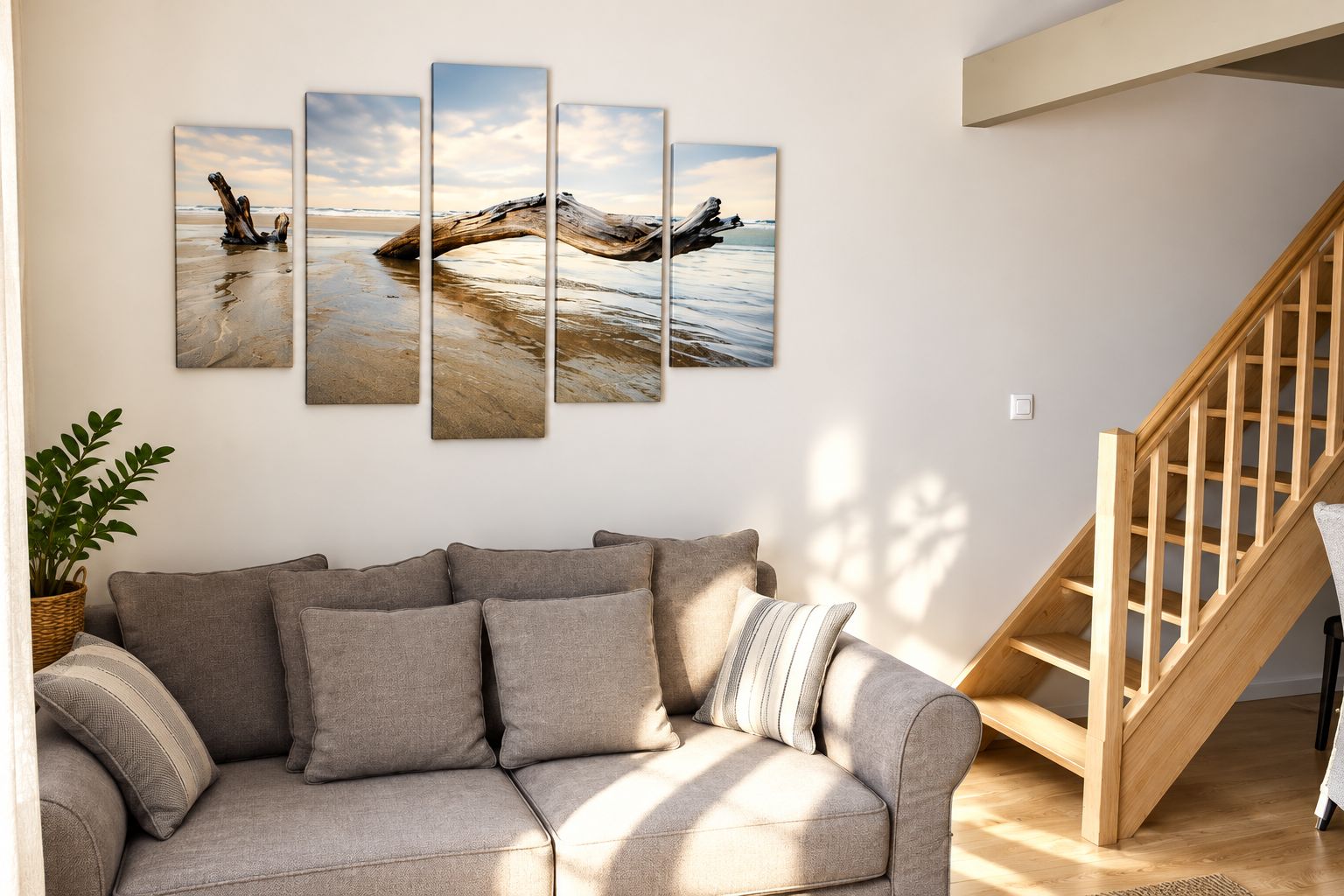A living room with a grey sofa, a wooden staircase, and a wall-mounted multi-panel artwork.
