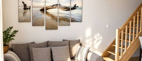 A living room with a grey sofa, a wooden staircase, and a wall-mounted multi-panel artwork.