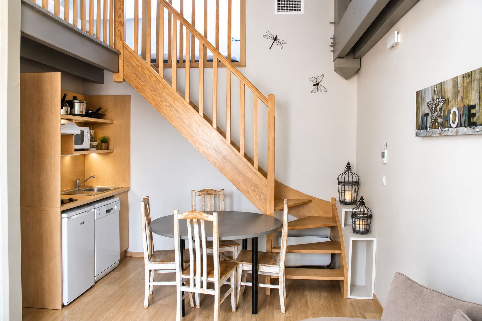 A modern kitchen with wooden cabinetry, a dining table with chairs, a wooden staircase, and decorative wall art.