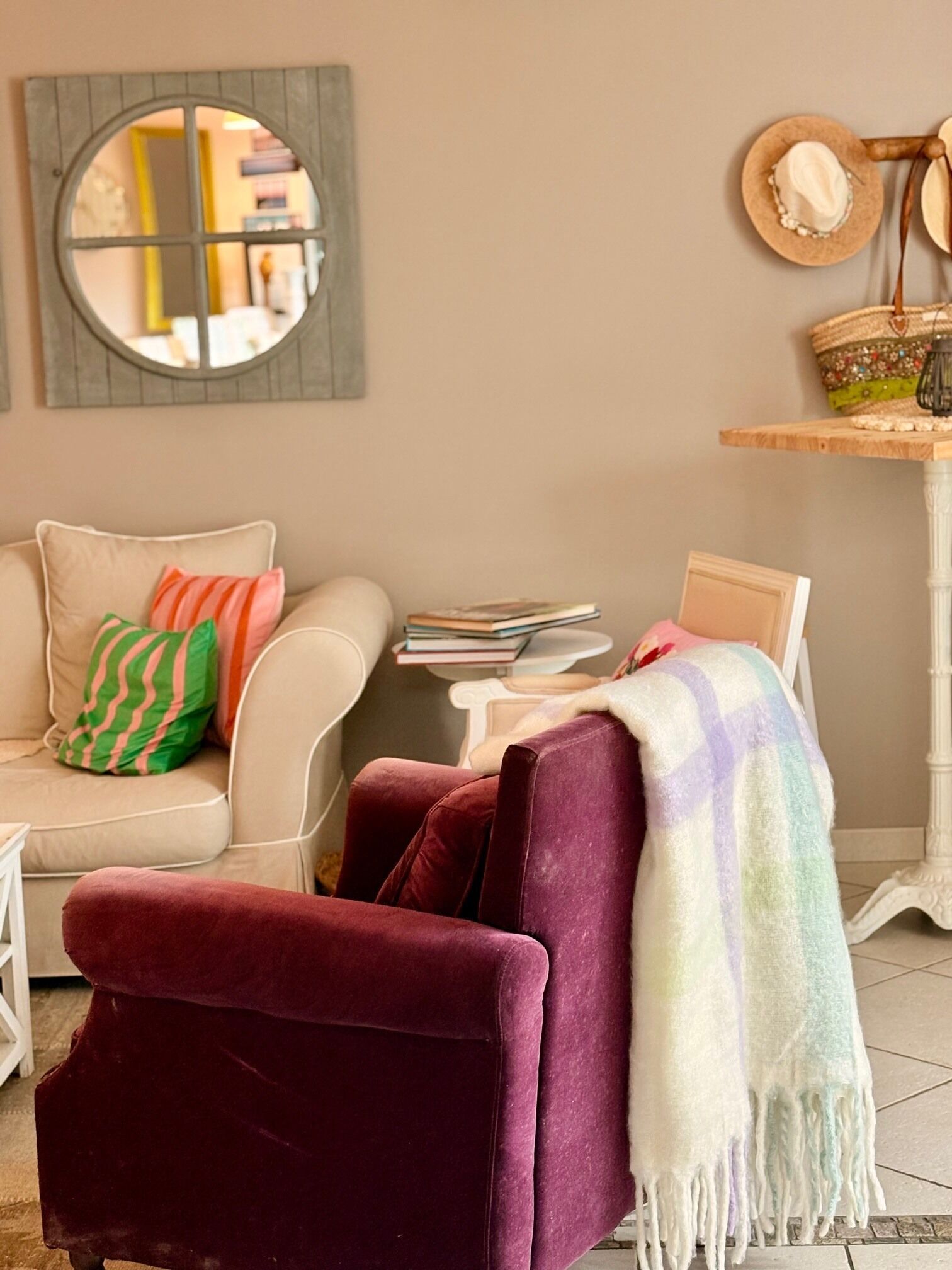 Un salon comprenant un canapé, un fauteuil, un miroir rond, une table avec des livres et un objet décoratif accroché au mur.