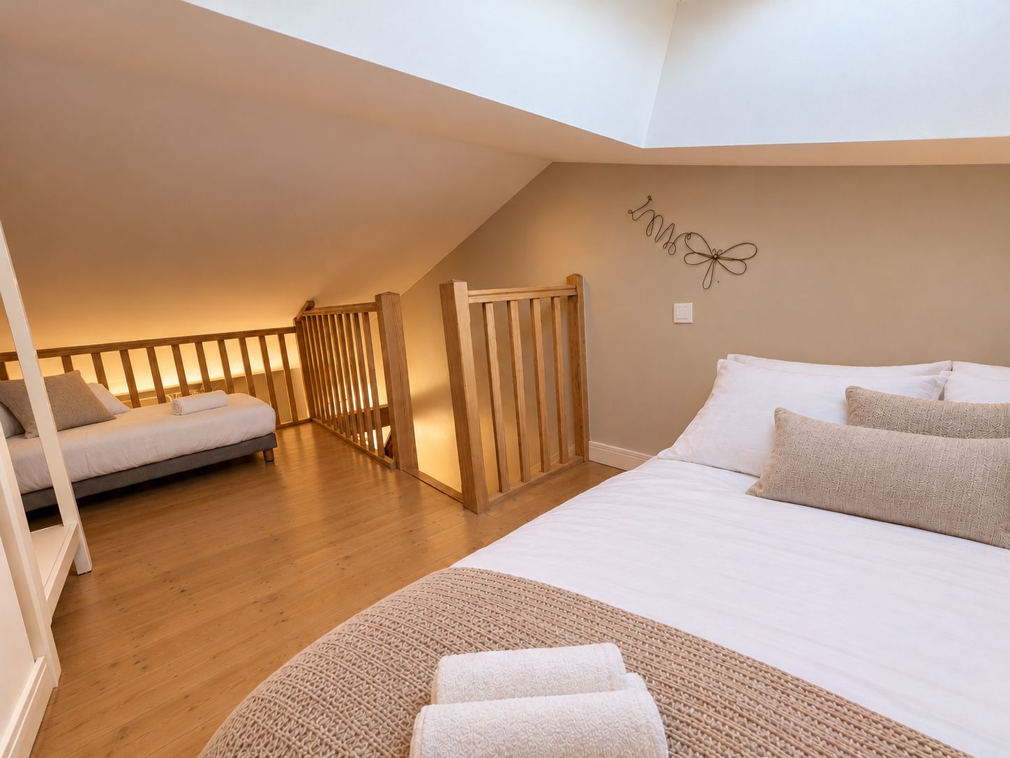 A bedroom with a loft-style design, featuring a large bed, a smaller bed, wooden railings, and a decorative wall piece.