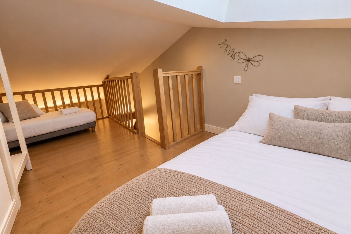 A bedroom with a loft-style design, featuring a large bed, a smaller bed, wooden railings, and a decorative wall piece.