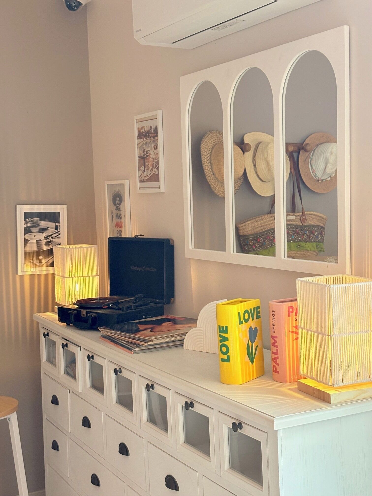A room with a white dresser, a record player, hats, and a framed picture on the wall.