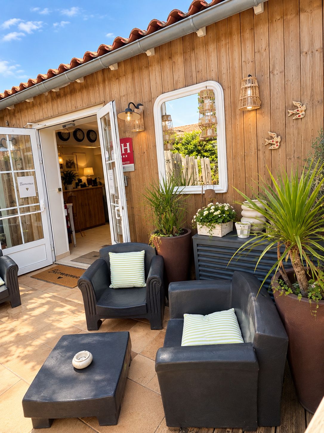 Un espace extérieur aménagé avec deux canapés et une table basse, un mur en bois avec une fenêtre et des plantes en pot.