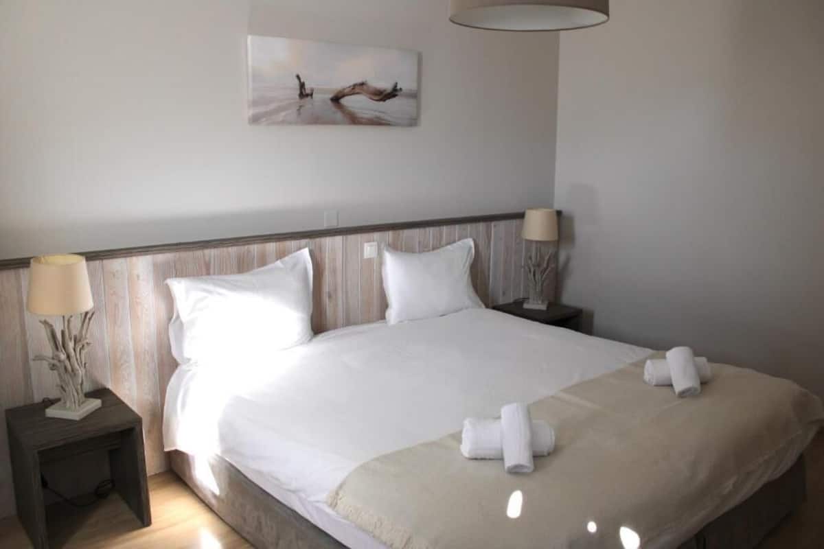 A hotel room with a bed, two bedside lamps, a wall-mounted painting, and a small table with a lamp.