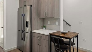 Une cuisine compacte dotée d’un réfrigérateur encastré, d’un petit plan de travail et d’une table en bois avec des chaises.