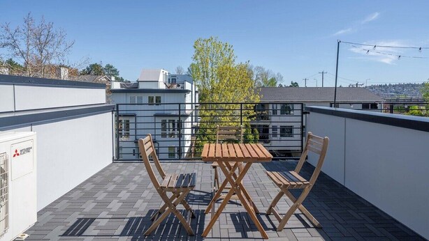 Une terrasse sur le toit, avec une table et des chaises, un climatiseur Mitsubishi Electric, et une vue sur les bâtiments et les arbres.