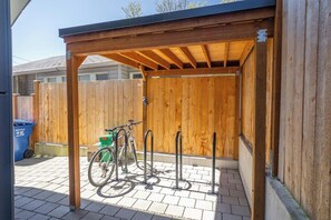 A covered outdoor area with a wooden fence, a bicycle rack, and a recycling bin. - Brand New 2BR Townhome in Fremont | Rooftop Patio (Seattle)
