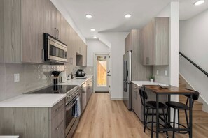 A modern kitchen with wooden cabinets, stainless steel appliances, and a central island with bar stools. - Brand New 2BR Townhome in Fremont | Rooftop Patio (Seattle)