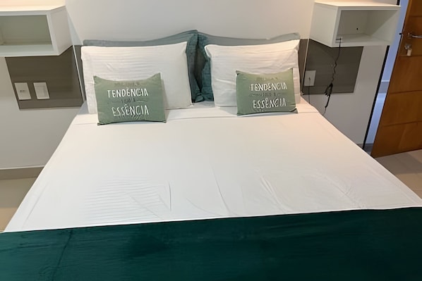 Uma cama com duas almofadas rotuladas 'TENDO ENGLIA ESSENCIA' e um edredom branco.