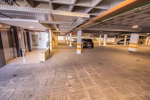Een parkeergarage met betonnen pilaren, een auto in de verte en een gebouwdeur links.