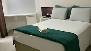 A neatly made bed with a green bedspread, a bedside table with a phone, and a window with curtains. - Gold Flat - Bela Vista (João Pessoa)