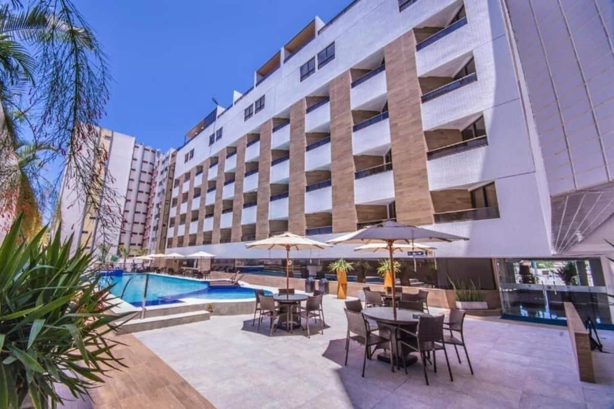 A hotel with a pool, outdoor seating, and a modern building facade.
