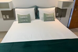 A bed with two pillows labeled 'TENDO ENGLIA ESSENCIA' and a white bedspread. - Gold Flat - Bela Vista (João Pessoa)