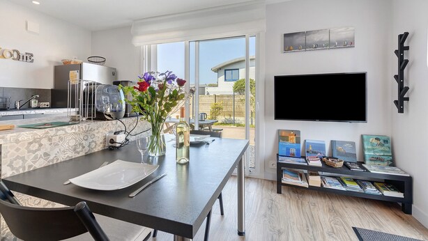 A modern kitchen with a dining area, a TV, and a bookshelf with books. - Ty An Heol Cottage: Private Terrace & Wi-Fi in Le Conquet, Brittany (Le Conquet)