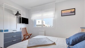 A bedroom with a bed, a chair, a dresser, a television, a window, and a picture on the wall. - Ty An Heol Cottage: Private Terrace & Wi-Fi in Le Conquet, Brittany (Le Conquet)
