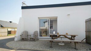 A patio with a wooden table and chairs, a sliding glass door, and a white exterior wall. - Ty An Heol Cottage: Private Terrace & Wi-Fi in Le Conquet, Brittany (Le Conquet)