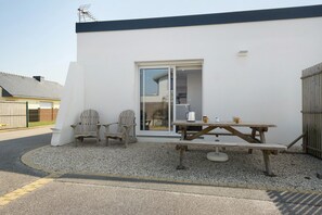 A patio with a wooden table and chairs, a sliding glass door, and a white exterior wall. - Ty An Heol Cottage: Private Terrace & Wi-Fi in Le Conquet, Brittany (Le Conquet)