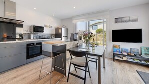 A modern kitchen with a built-in oven, microwave, and a dining area with a table and chairs. - Ty An Heol Cottage: Private Terrace & Wi-Fi in Le Conquet, Brittany (Le Conquet)
