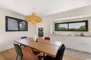 Une cuisine moderne avec un coin repas, comprenant une table en bois, des chaises, un luminaire suspendu et une fenêtre offrant une vue agréable.