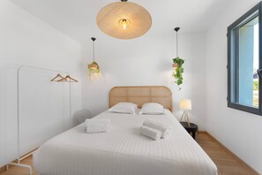 Une chambre à coucher bien aménagée, avec un grand lit, un luminaire suspendu, une table de chevet avec une lampe et une fenêtre donnant sur un beau paysage.