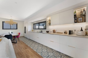 A modern kitchen with white cabinetry, a large window, and a dining area with a table and chairs. - Villa 'Laross' with Private Garden and Wi-Fi (Gujan-Mestras)