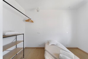 Une pièce minimaliste avec un lit superposé, une étagère en bois, un luminaire suspendu et un cintre en bois.