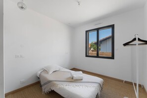 A bedroom with a bed, a window with a view, and a clothing rack. - Villa 'Laross' with Private Garden and Wi-Fi (Gujan-Mestras)