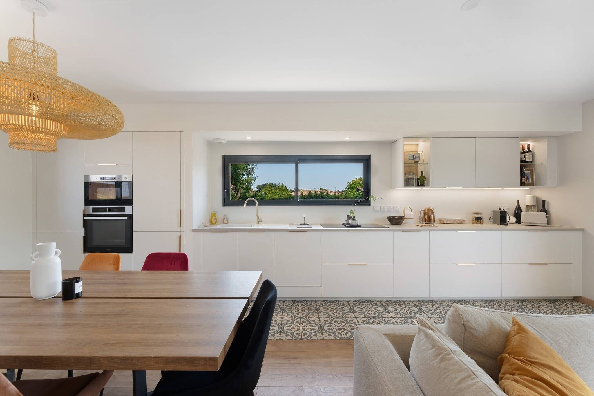 Una cocina moderna con armarios blancos, horno empotrado y ventana con vistas a zonas verdes.