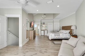 Ein geräumiges Schlafzimmer mit einem großen Bett, einem Nachttisch, einer Kommode und einem Deckenventilator.
