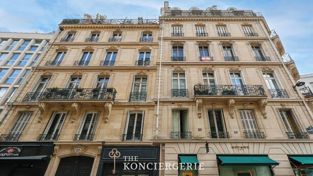 Un edificio de varios pisos con estilo arquitectónico clásico, que presenta balcones ornamentados y un escaparate destacado con señalización.