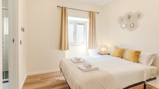A bedroom with a bed, curtains, a wall decoration, and a bedside table with a lamp. - #379 Sunny Corner | Albufeira Stay (Albufeira)